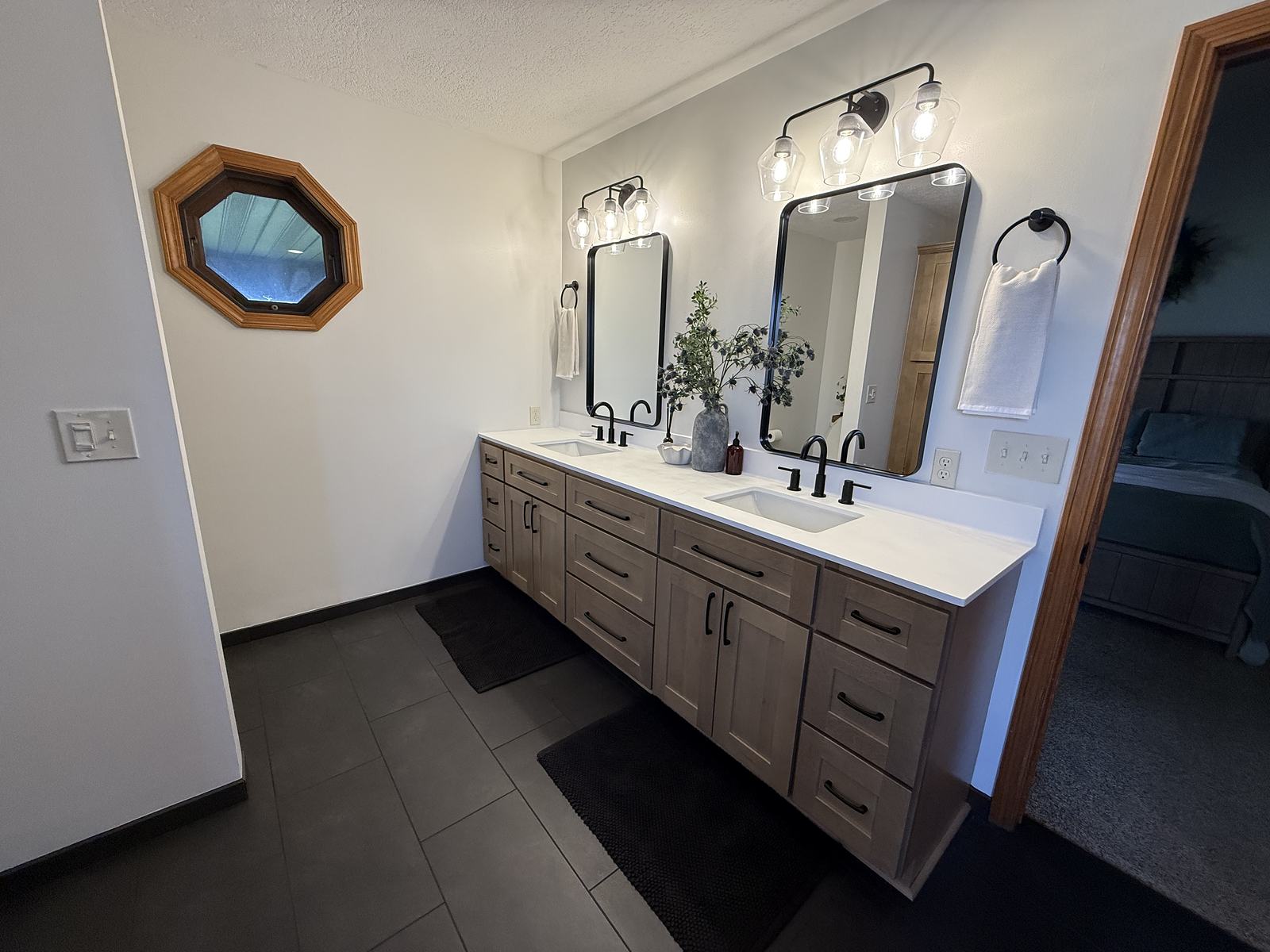 Greige stained double vanity with black fixtures and charcoal tile floor