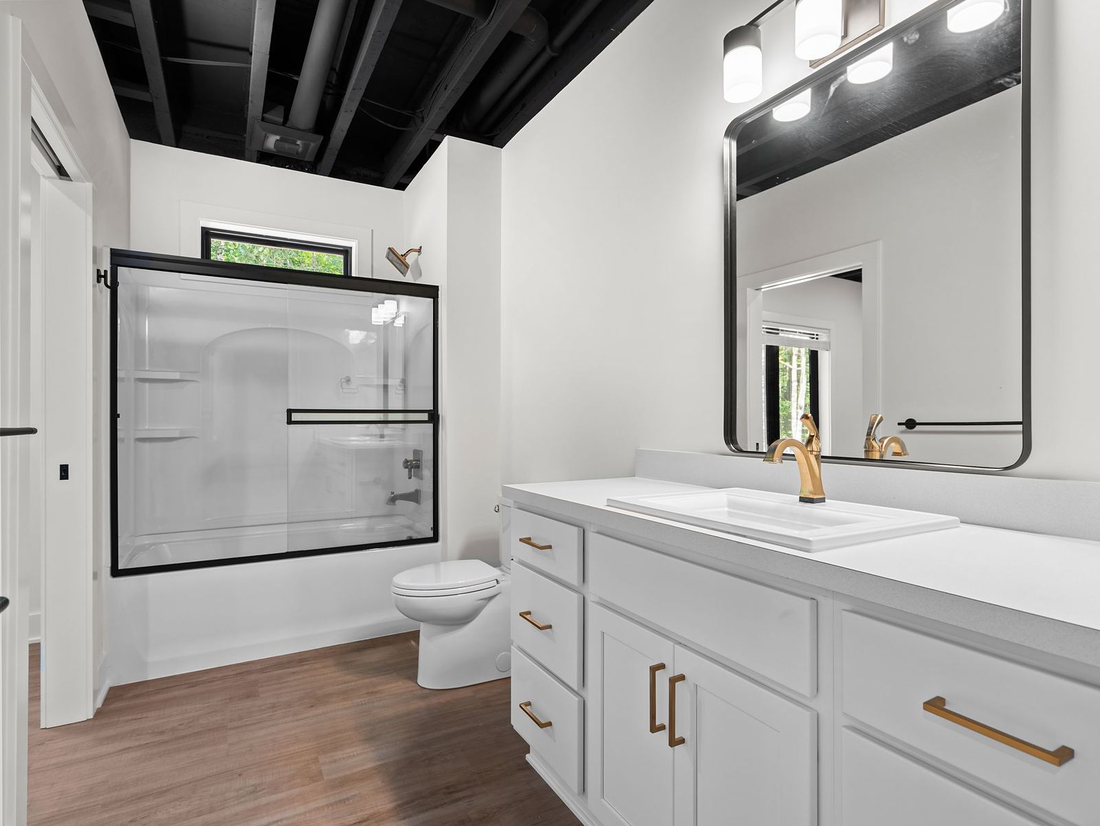 Lower-level bath with a white vanity, gold fixtures and exposed black ceiling
