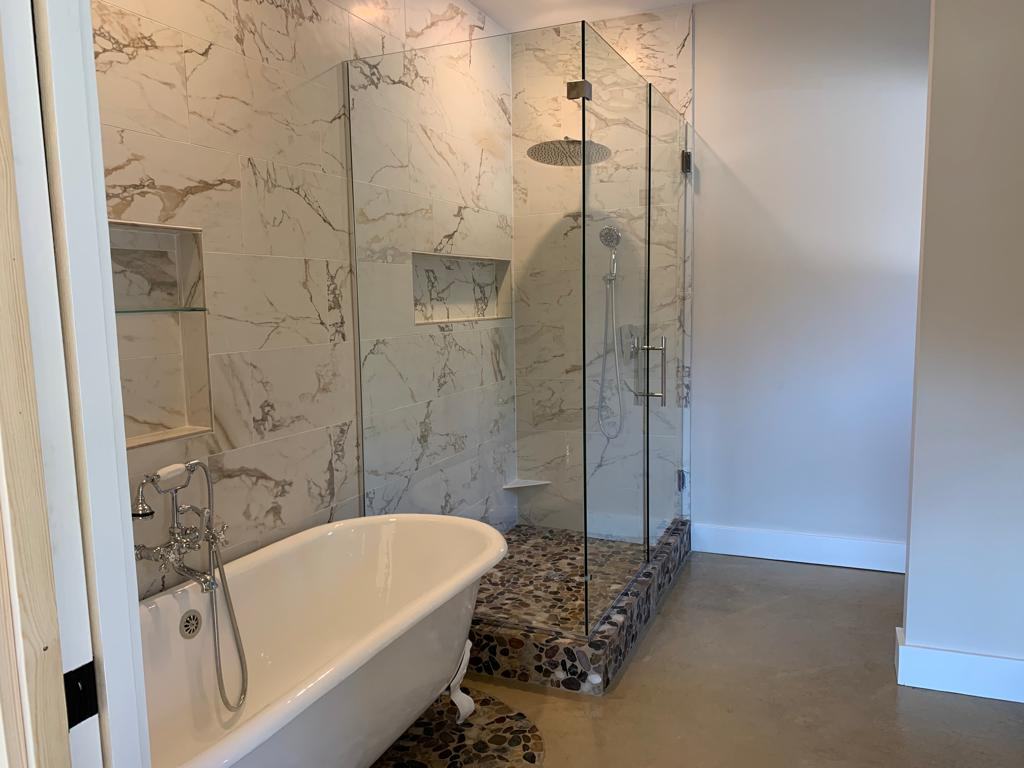 Marble-tile walk-in shower with a pebble floor beside a clawfoot tub