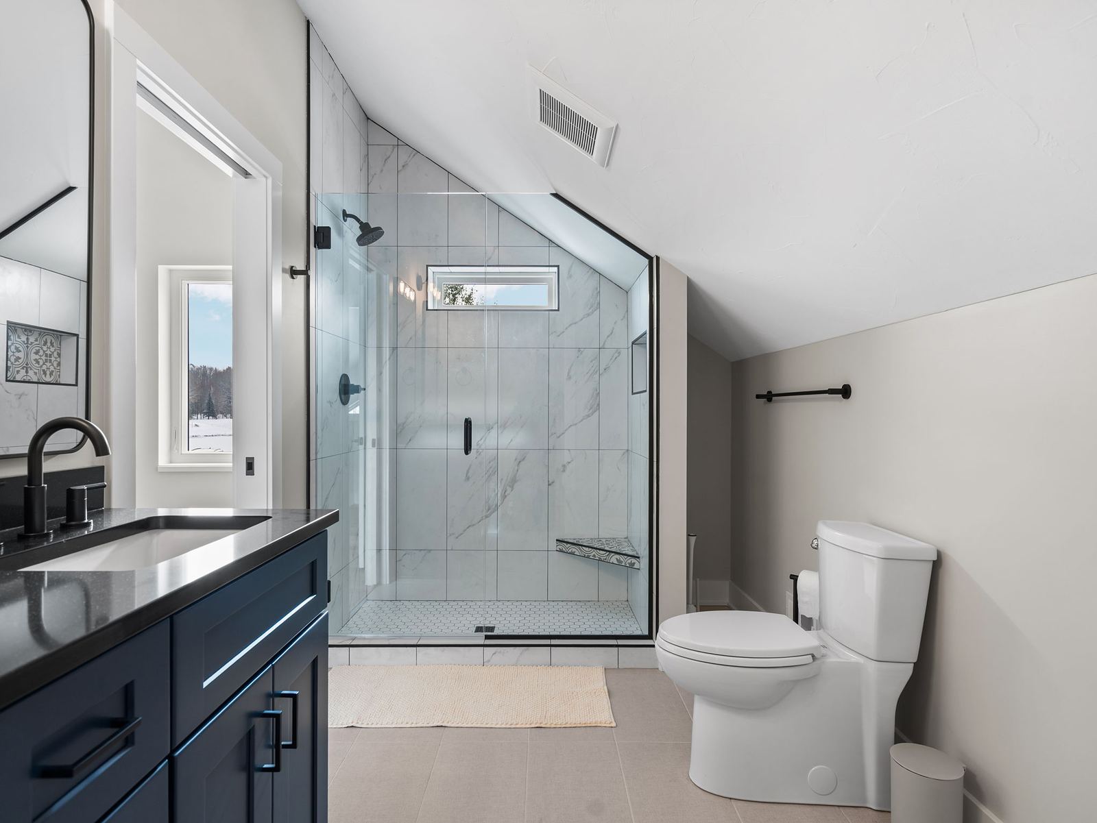 Bath with a navy vanity, black quartz top and marble-tile shower