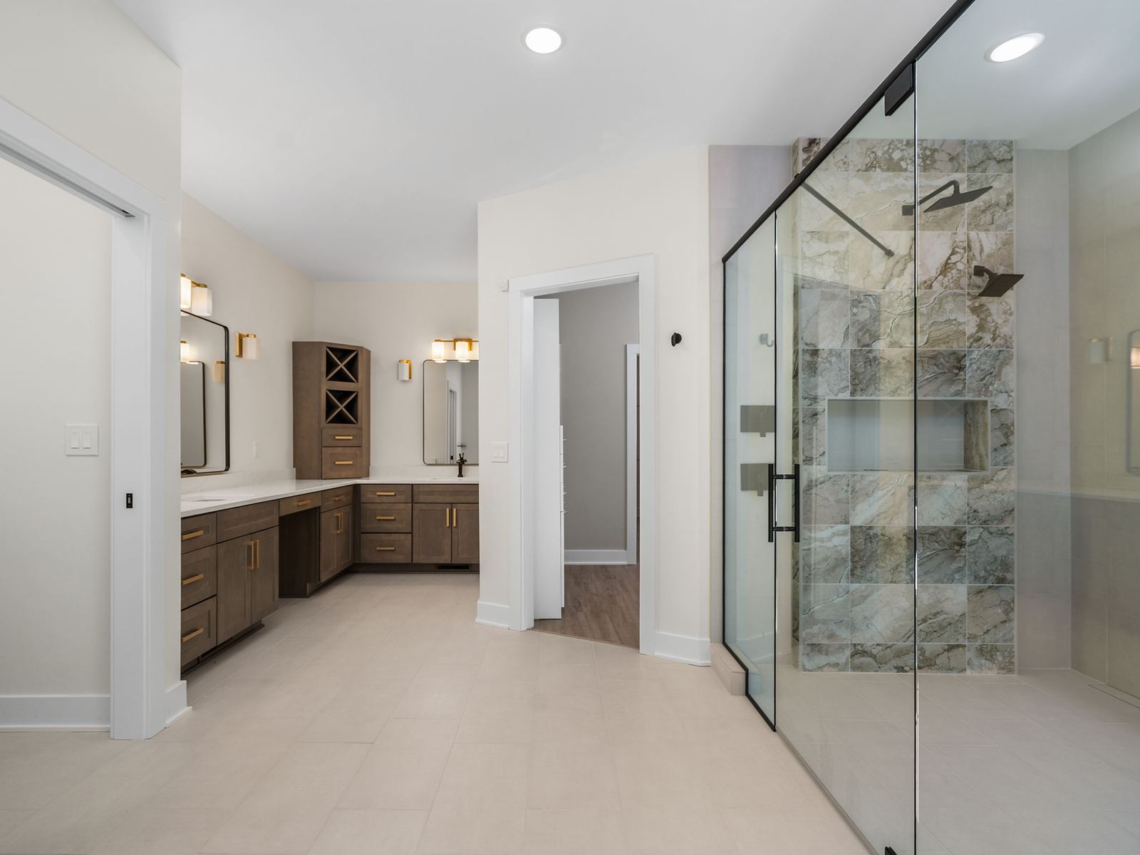 Primary bath with a marble-tile shower, double vanity and brushed brass sconces