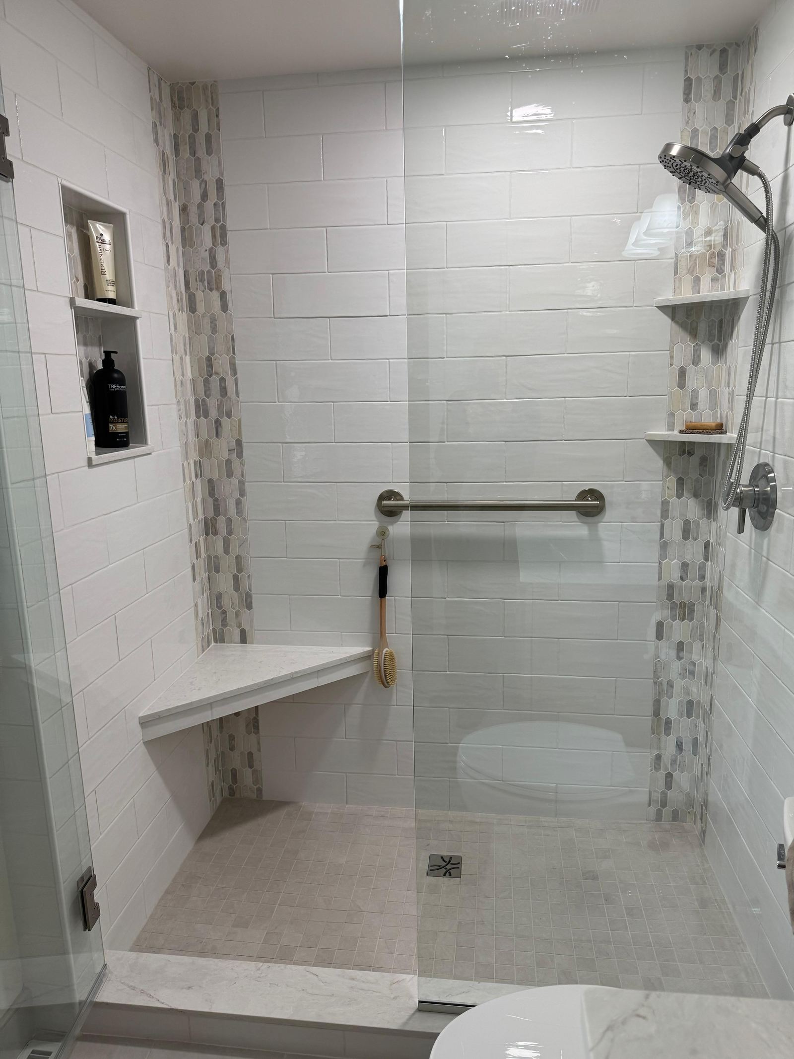 White tile shower with a hexagonal mosaic accent, marble bench and niche