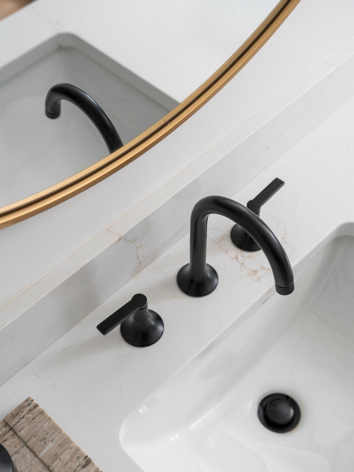 Matte black widespread faucet on a quartz vanity below a brass mirror