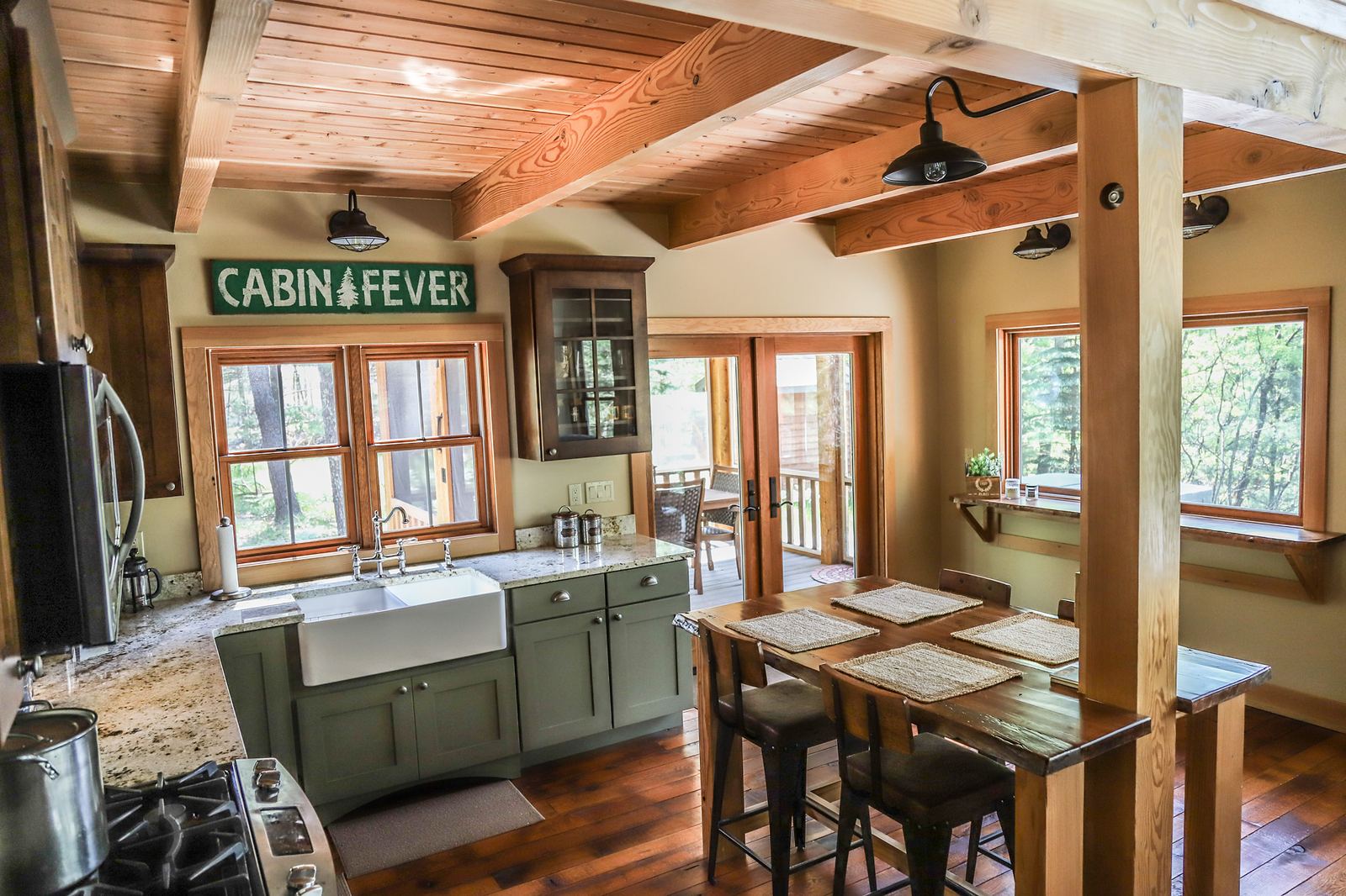 Cabin kitchen with sage cabinets, a farmhouse sink, granite counters and exposed timber beams
