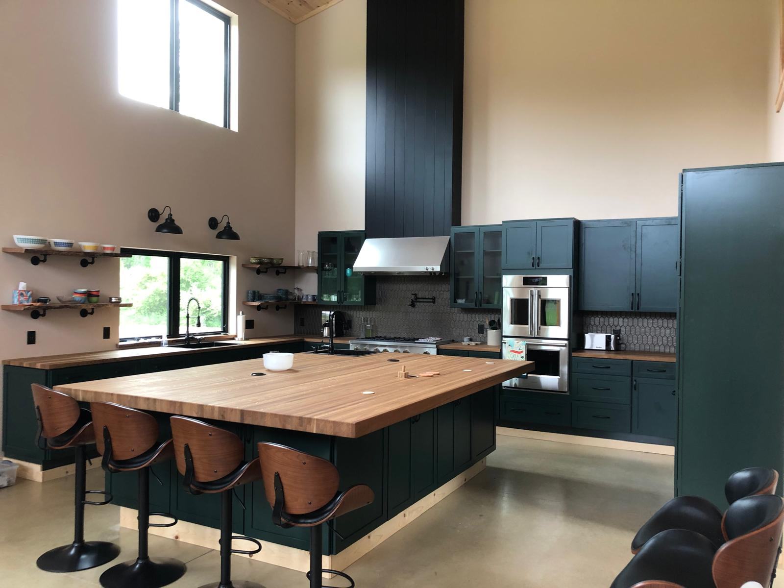Forest green kitchen with a butcher block island and a two-storey shiplap hood