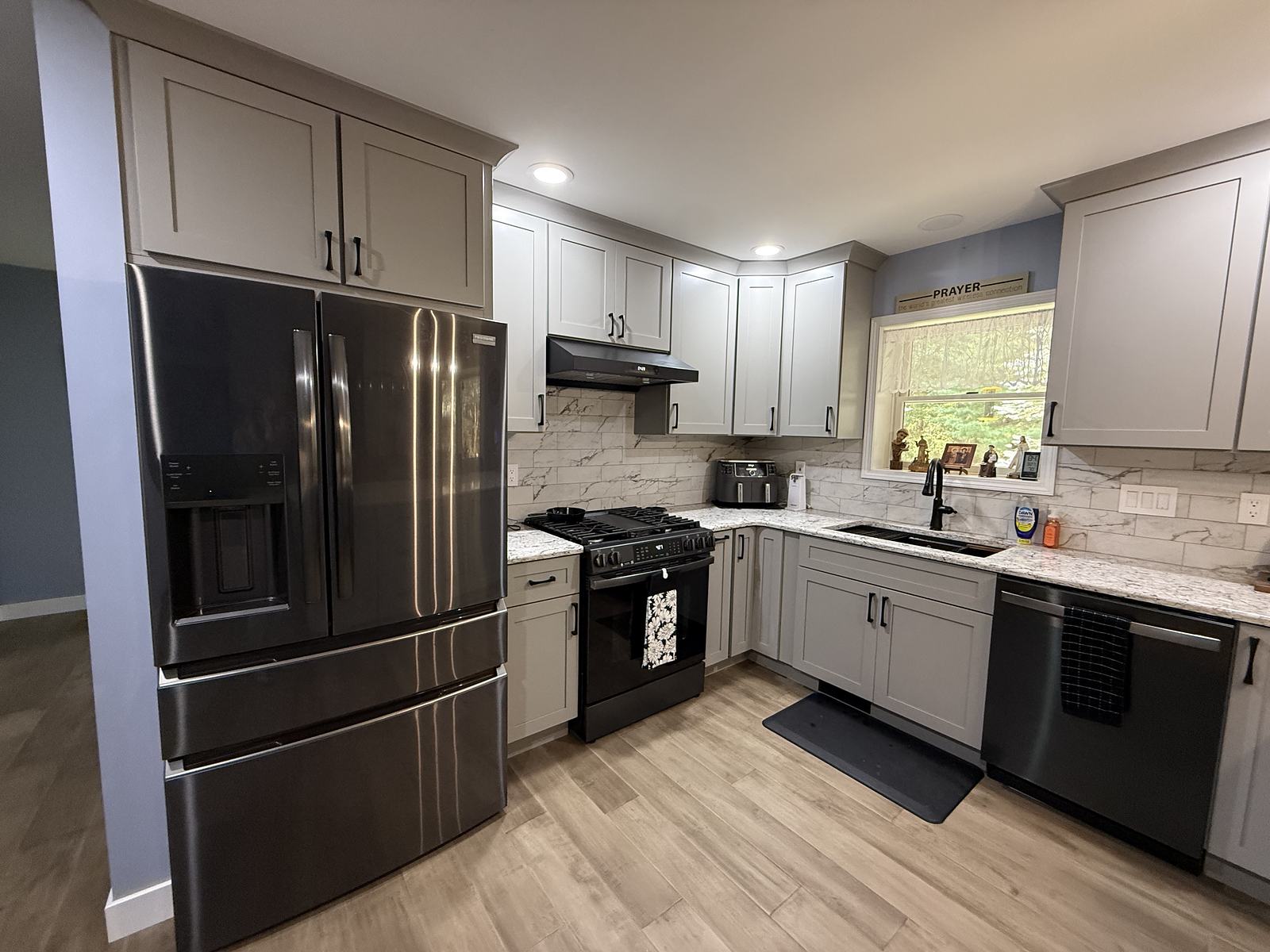 Grey shaker kitchen with black stainless appliances and a marble-look tile backsplash