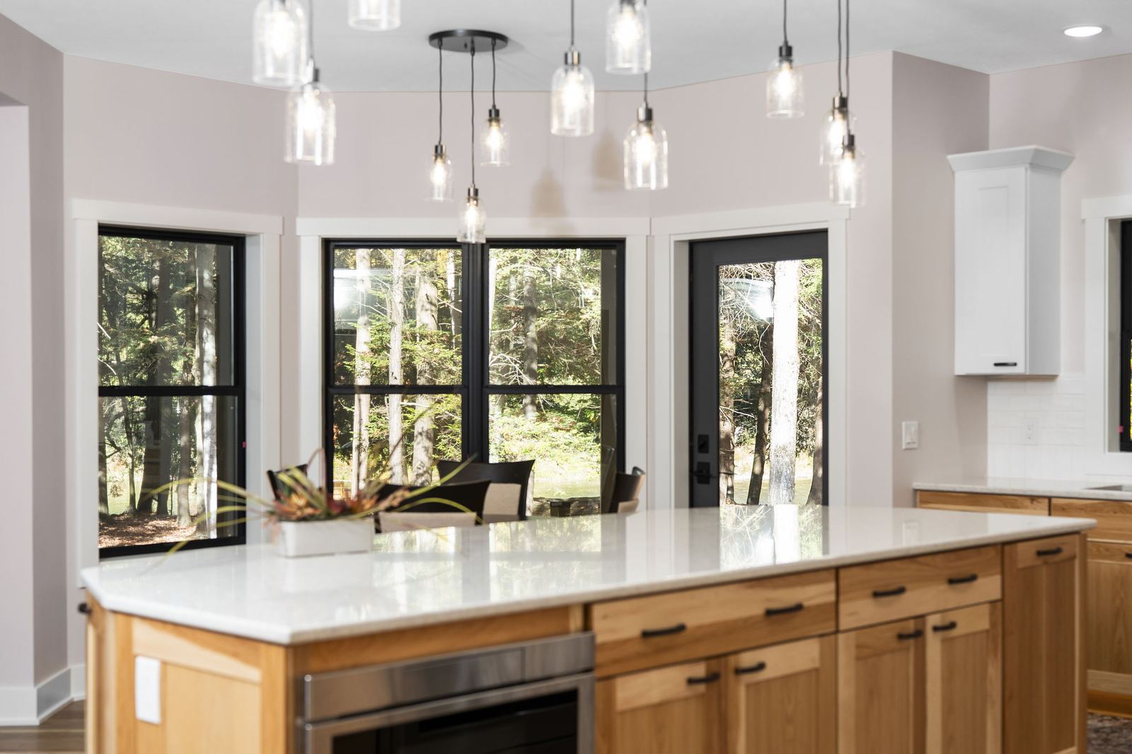 Hickory island under glass pendants, framed by black-trim forest windows
