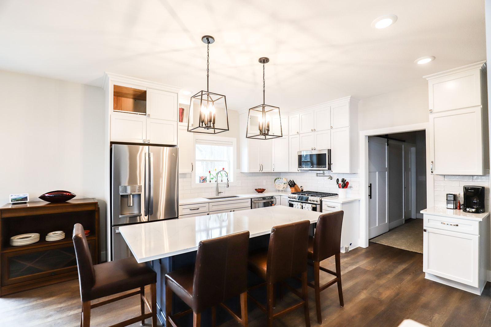 White kitchen with a dark island, lantern pendants and leather counter stools