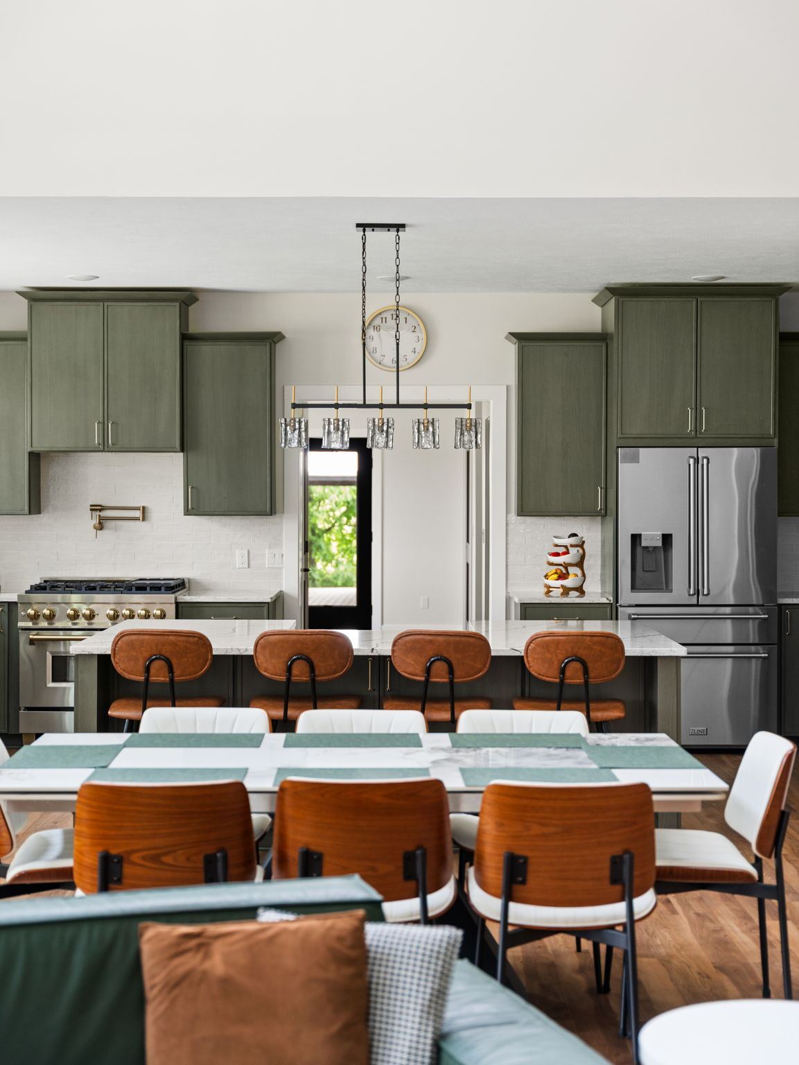 Olive green kitchen with a marble island, leather stools and a pro range