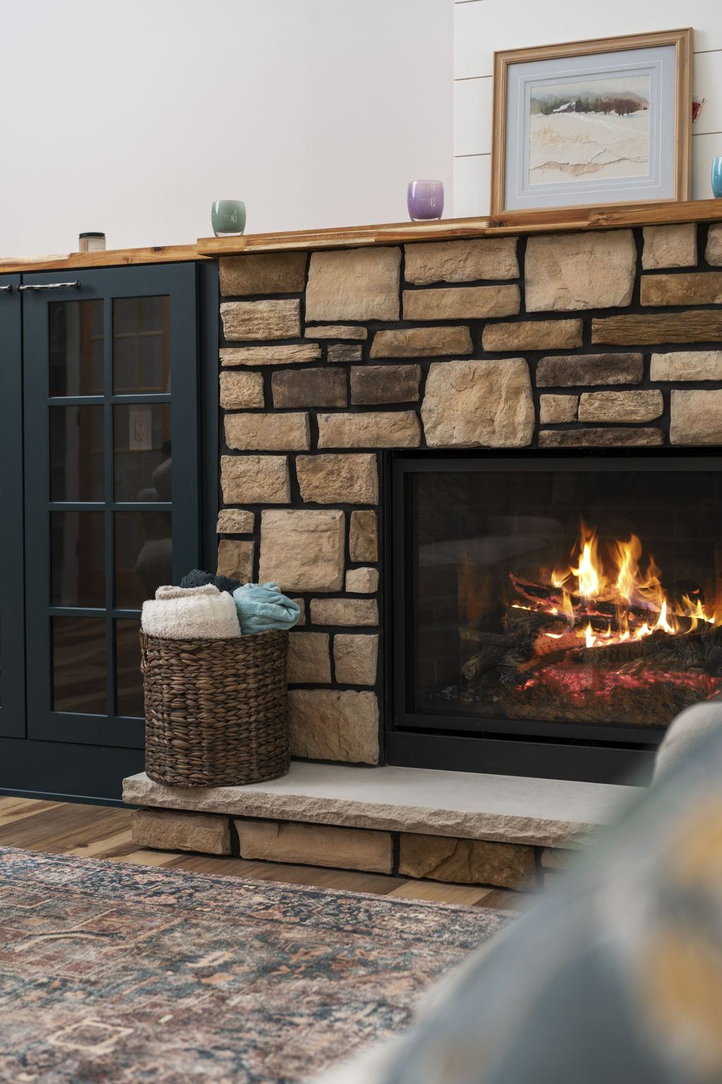 Stone fireplace detail with a live-edge mantel and navy glass-front cabinets