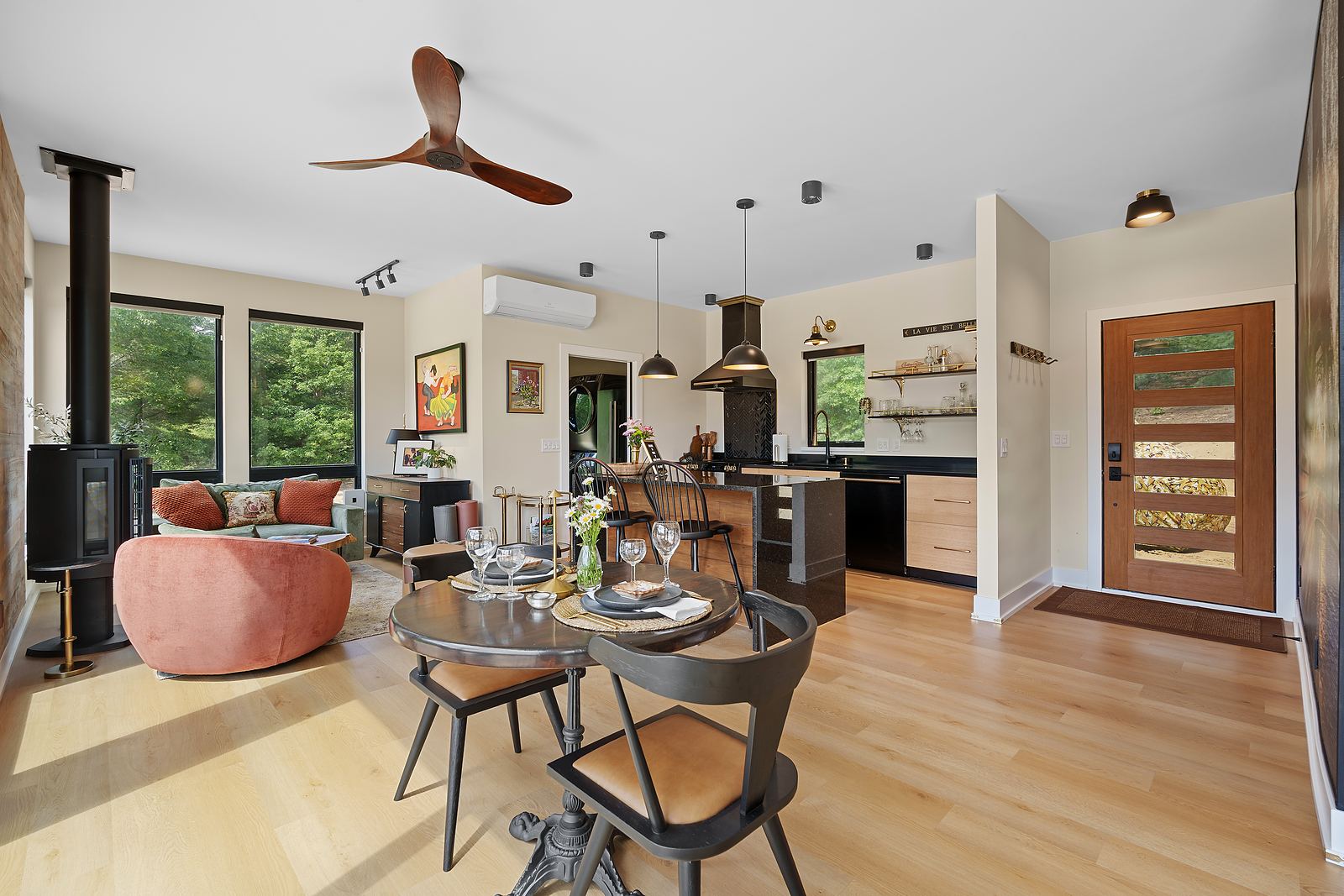 Open living and dining space with a wood stove, white oak floors and a modern entry door