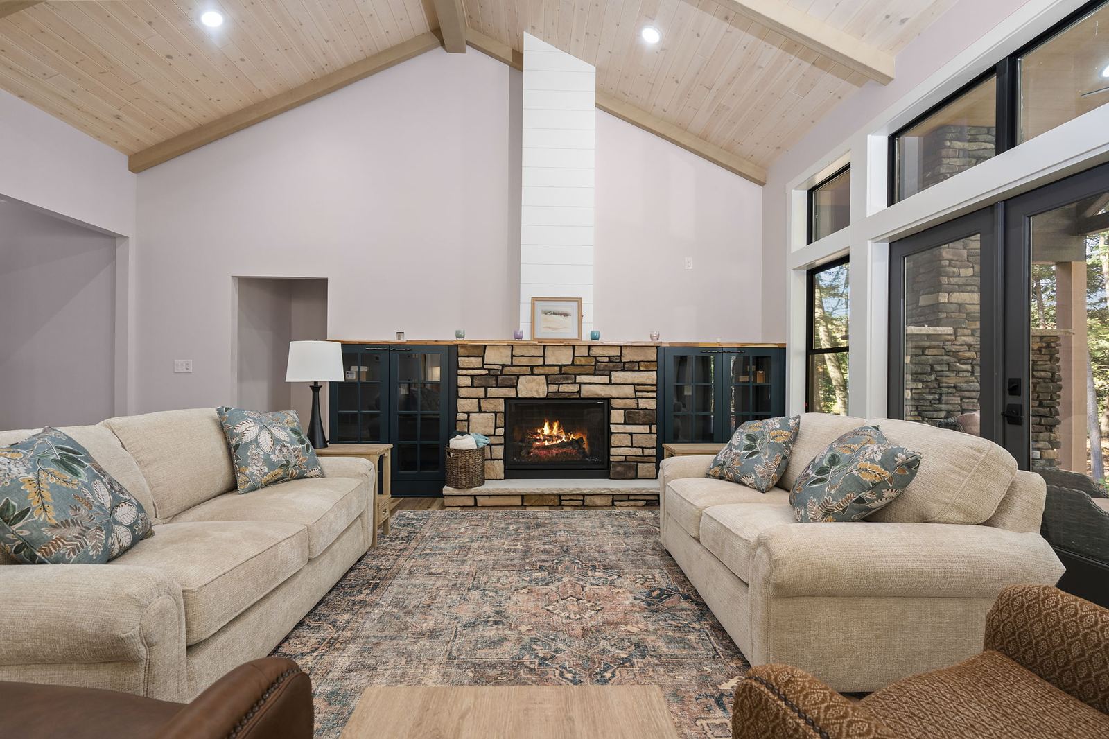 Great room with a stone fireplace, vaulted wood ceiling and navy built-in cabinets