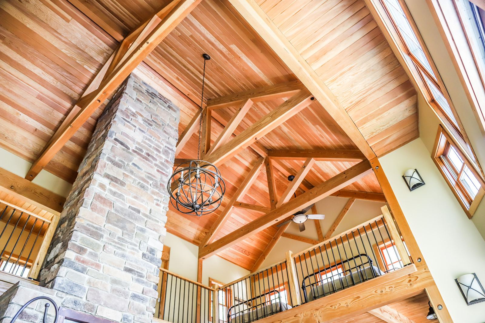 Vaulted great room with exposed timber trusses, a stone chimney and loft rail