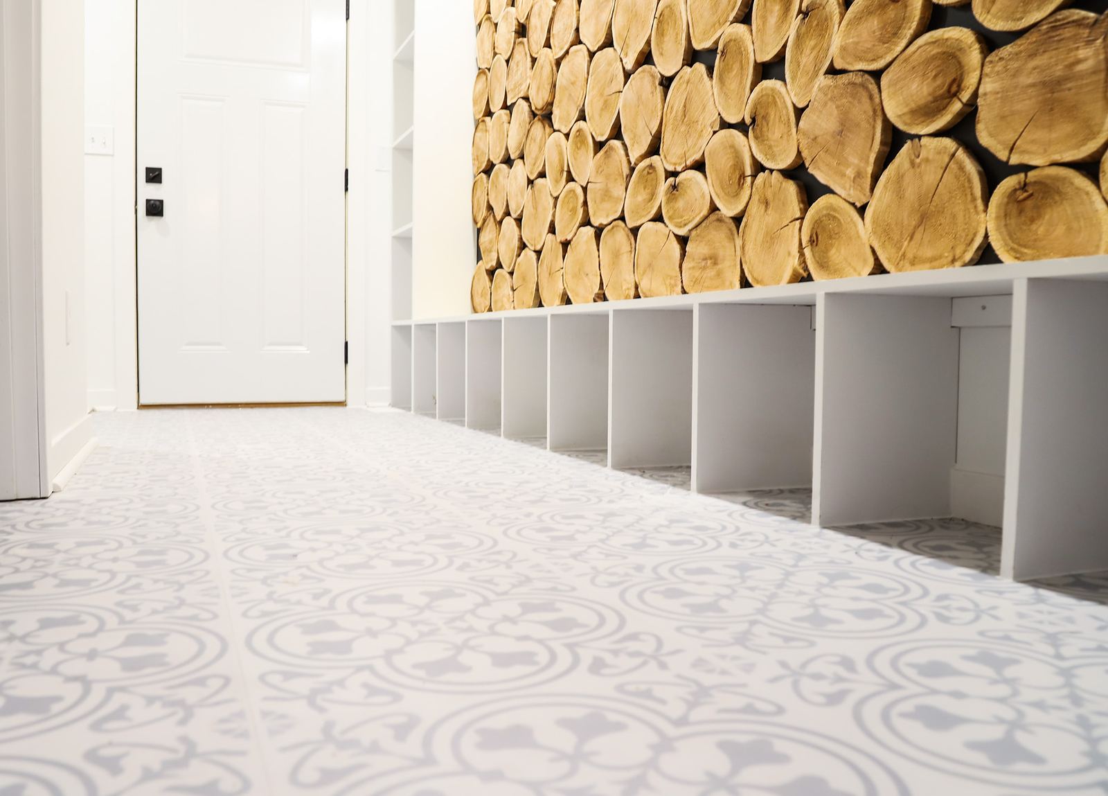Mudroom with white cubby lockers, a stacked log feature wall and patterned tile floor