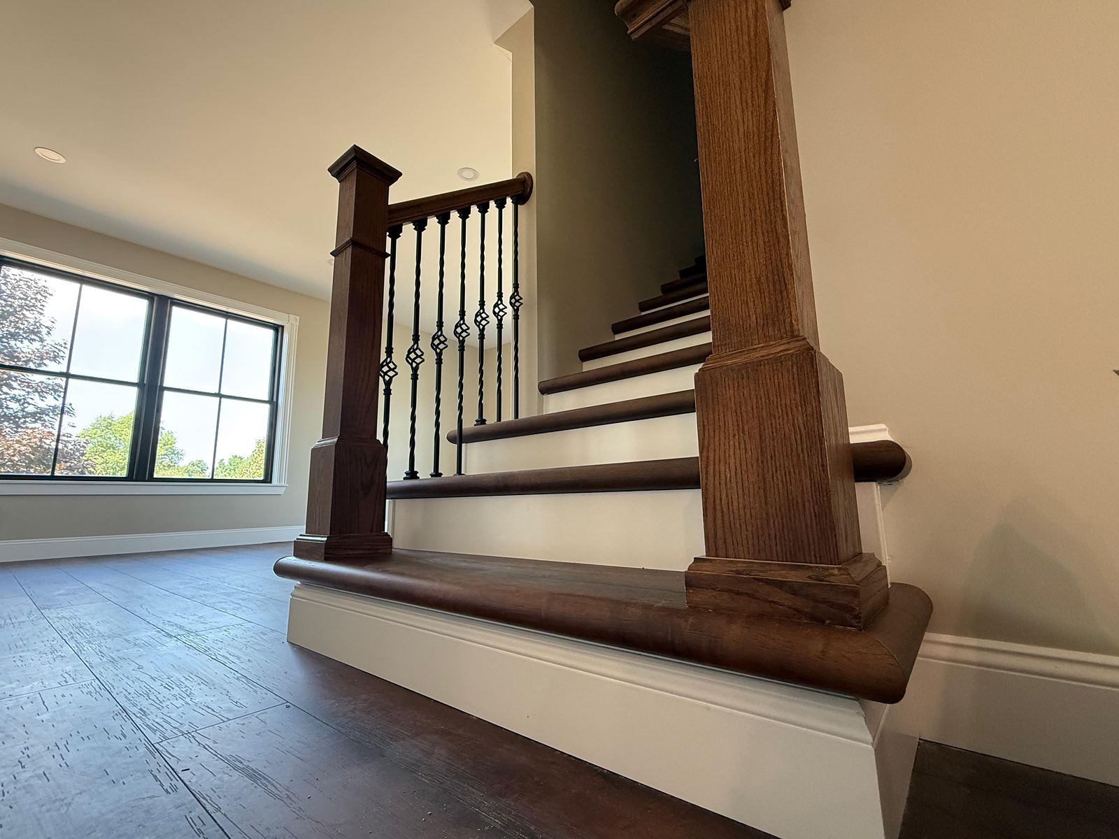 Oak staircase with wrought iron balusters, boxed newels and dark wide-plank floors